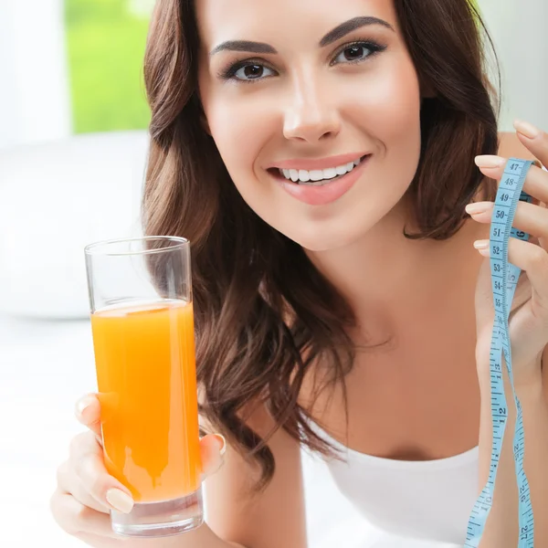 Mujer con jugo de naranja y cinta métrica, en el interior —  Fotos de Stock