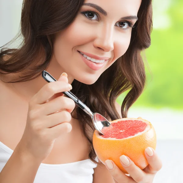 Lachende jonge vrouw eten grapefruit thuis — Stockfoto