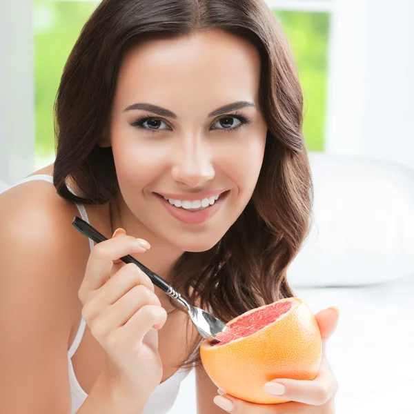 Usměvavá mladá žena doma jíst grapefruit — Stock fotografie