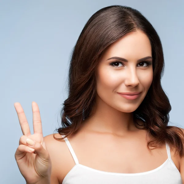 Woman showing two fingers or victory gesture, on grey — Stock Photo, Image