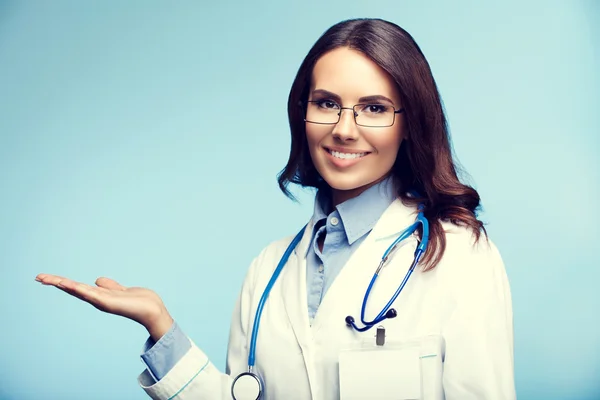 Young doctor showing something, on blue — Stock Photo, Image