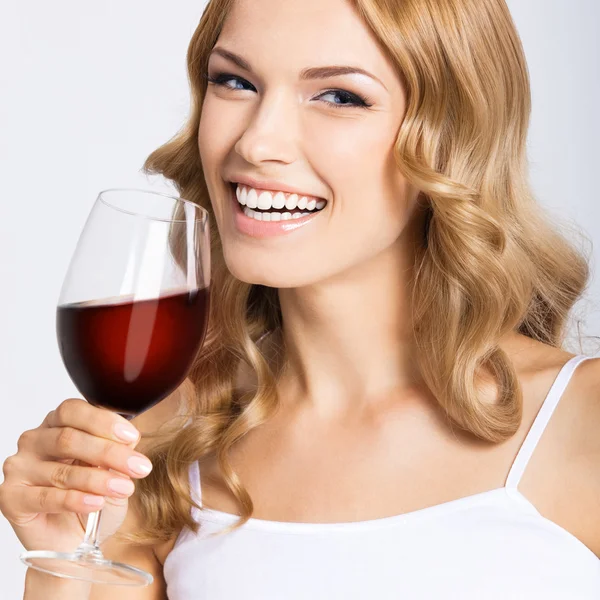 Junge glückliche Frau mit einem Glas Rotwein, auf grau — Stockfoto
