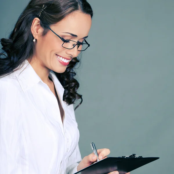 Businesswoman with clipboard writing, on gray — Stock Photo, Image