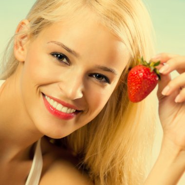 Genç gülümseyen kadın plajda çilek ile