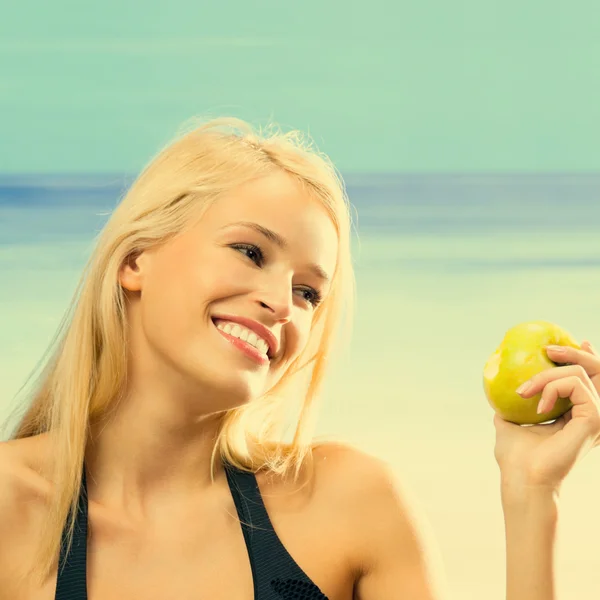 Jovem mulher sorridente com maçã na praia — Fotografia de Stock