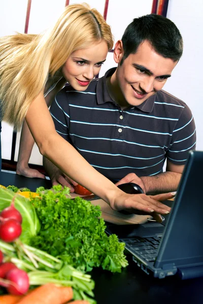 Joven pareja feliz cocina en la cocina con el ordenador portátil — Foto de Stock