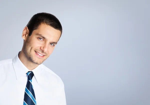 Happy smiling young businessman, against grey — Stock Photo, Image