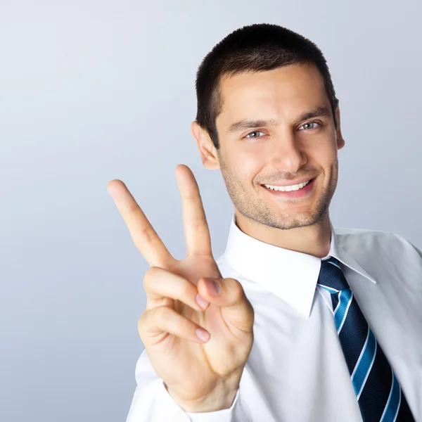 Businessman showing two fingers, against grey — Stock Photo, Image