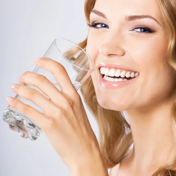 Joven mujer feliz bebiendo agua, sobre gris — Foto de Stock