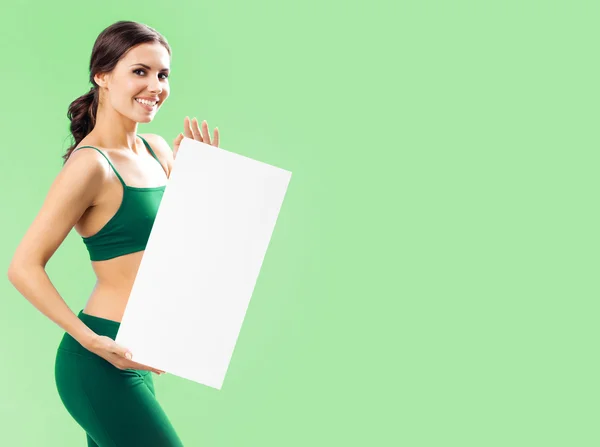 Woman in fitnesswear showing signboard, on green — Stock Photo, Image