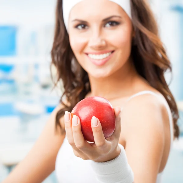 Счастливая женщина дарит красное яблоко, в фитнес-центре — стоковое фото