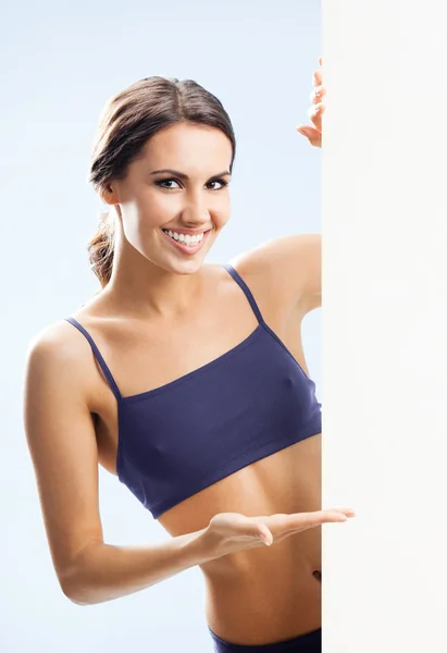 Woman in fitnesswear showing signboard, over grey — Stock Photo, Image