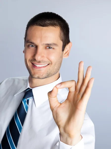 Χαμογελώντας επιχειρηματίας δείχνει εντάξει χειρονομία, ενάντια σε γκρι — Φωτογραφία Αρχείου