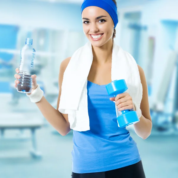 Woman in blue sportswear with bottle of water and dumbbell, at f — Zdjęcie stockowe