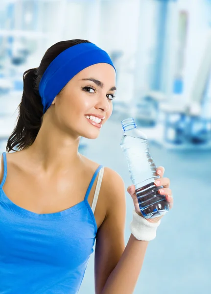 Mujer sonriente en ropa deportiva agua potable, en el gimnasio — Foto de Stock