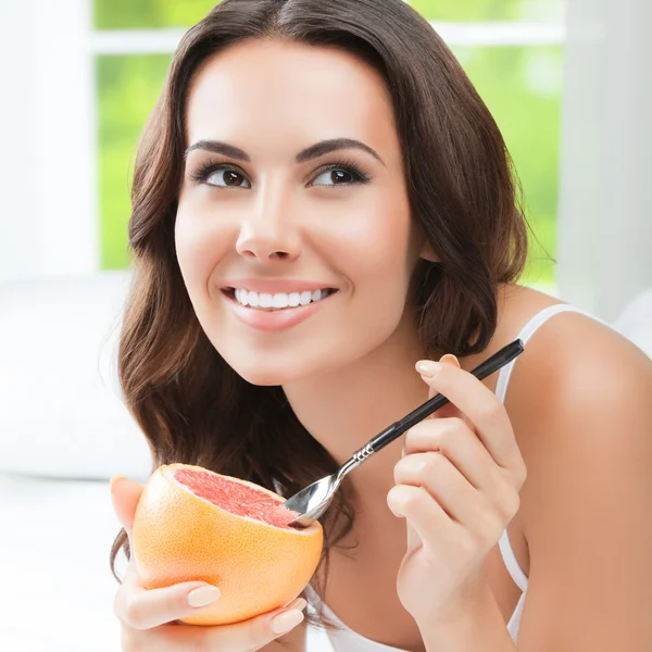 Usměvavá mladá žena doma jíst grapefruit — Stock fotografie