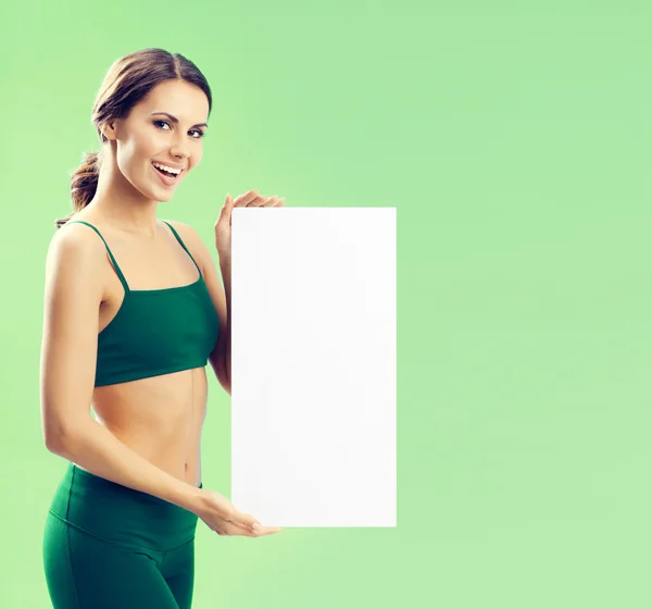 Young woman in fitnesswear showing signboard, on green — Stock Photo, Image