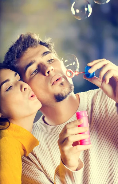 Young attractive happy couple blowing bubbles outdoors — Stock Photo, Image