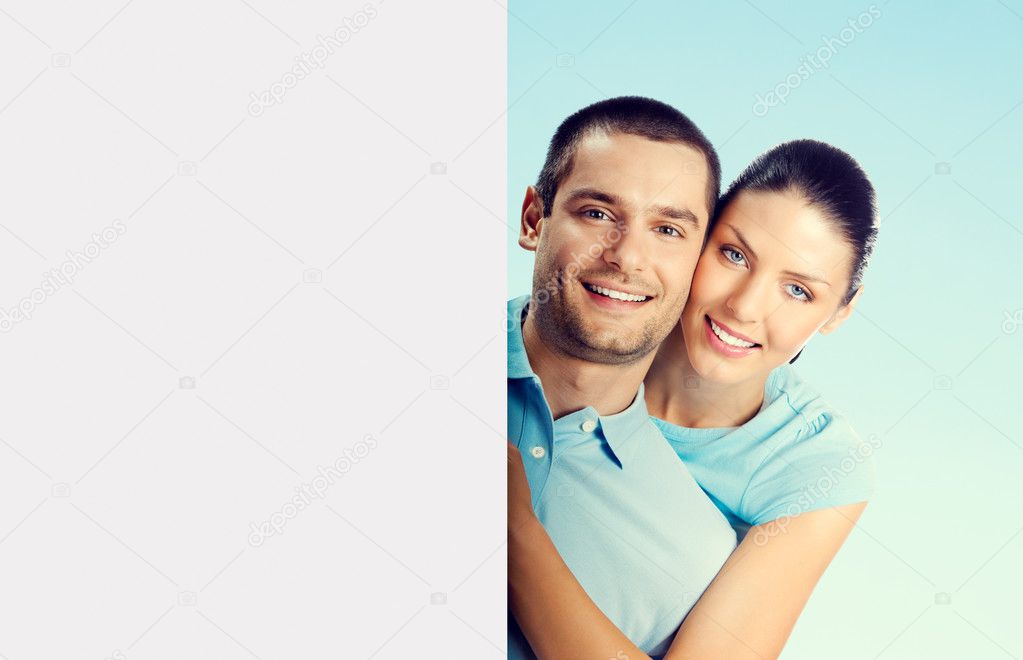 young attractive couple with blank signboard, on blue