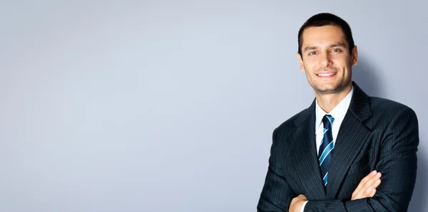 Feliz hombre de negocios con los brazos cruzados, contra gris — Foto de Stock