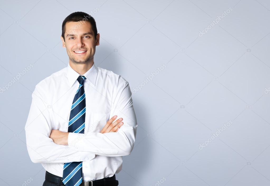 Happy smiling young businessman, against grey