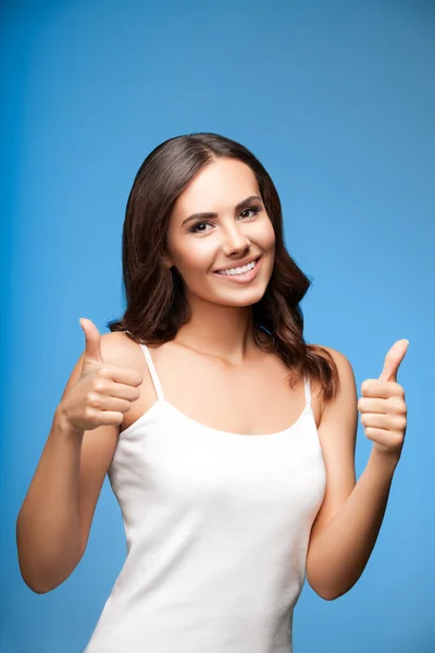 Mladá žena ukazuje palcem nahoru gesto, na modré — Stock fotografie