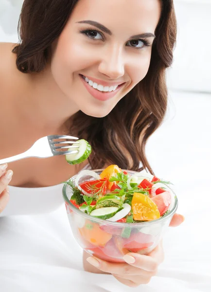 Lachende jonge vrouw eten Salade, op bed — Stockfoto