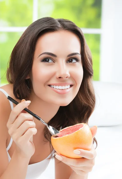 Mujer joven sonriente comiendo toronja en casa —  Fotos de Stock