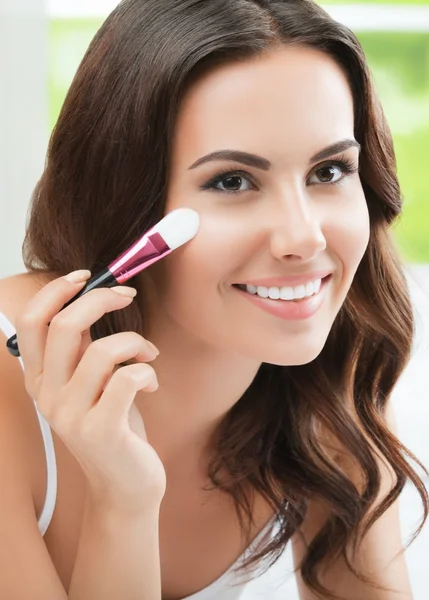 Mujer joven sonriente con cepillo de maquillaje, en el interior —  Fotos de Stock