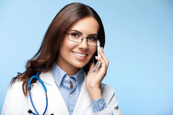 Jeune médecin souriant avec téléphone portable, sur bleu — Photo