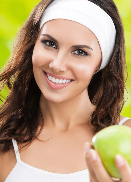 Молода усміхнена жінка в спортивному одязі з зеленим яблуком, відкритий — стокове фото