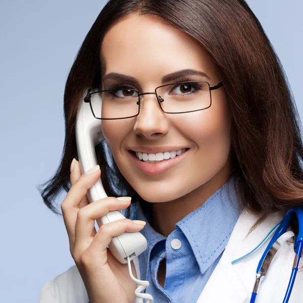 Jeune médecin souriant avec téléphone, sur gris — Photo