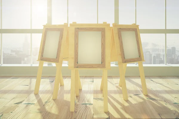 Пустая рамка на мольбертах в большой солнечной комнате с деревянным гриппом — стоковое фото