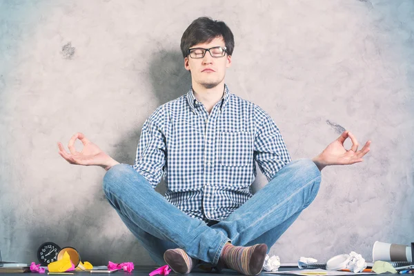 Handsome caucasian man meditating on messy desktop with concrete wall in the background — Stock Photo, Image