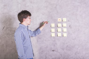 Genç Beyaz adam beton duvarla yanında ayakta çapraz ve çıkartmaları hakkında bir karar vermek için işaretleyin 