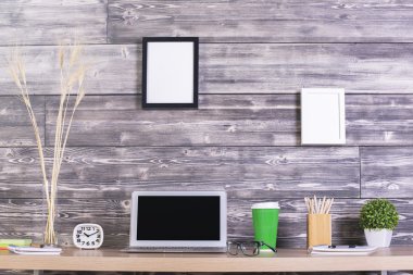 Boş dizüstü bilgisayar, saat, kahve ve diğer öğeler üzerinde ahşap duvarda asılı resim çerçeveleri ile yaratıcı tasarımcı tablo. Yukarı alay