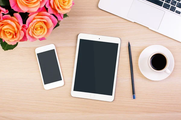 Güller, boş akıllı telefon ve tablet ekranları, kahve fincanı, kalem ve dizüstü bilgisayar klavyesi ile yaratıcı kadın masaüstü üst görünümü. Alay etmek