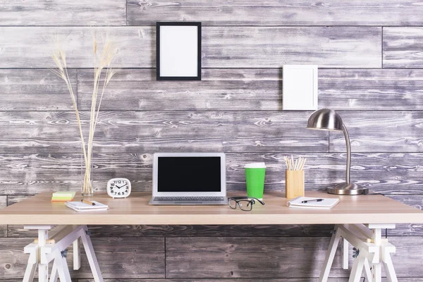 Mesa de designer criativo com laptop em branco, relógio, café e outros itens com molduras penduradas acima na parede de madeira. Faz asneira. — Fotografia de Stock