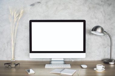 Boş beyaz bilgisayar monitörü, buğday sivri, gözlük, akıllı telefon, not defteri, kahve fincanı ve beton arka plan üzerinde lamba ile Yaratıcı masaüstü. Alay etmek