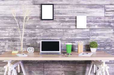 Boş dizüstü bilgisayar, saat, kahve ve diğer öğeler üzerinde ahşap duvarda asılı resim çerçeveleri ile yaratıcı tasarımcı masaüstüyle. Yukarı alay