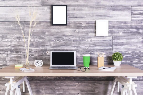 Designer criativo desktop com laptop em branco, relógio, café e outros itens com molduras penduradas acima na parede de madeira. Faz asneira. — Fotografia de Stock