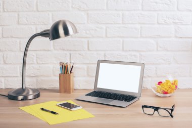 Yaratıcı tasarımcı masaüstü boş beyaz dizüstü, kırtasiye, Masa lambası, gözlük ve beyaz tuğla duvar arka plan üstünde smartphone ile.