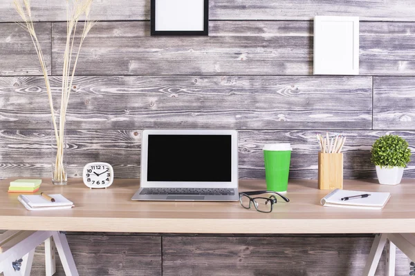 Kreativer Designer-Schreibtisch mit leerem Laptop, Uhr, Kaffee und anderen Artikeln mit Bilderrahmen, die oben an der Holzwand hängen. Attrappe — Stockfoto