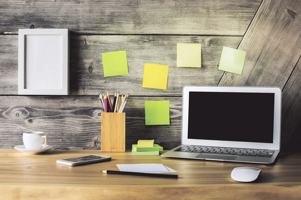 Creative designer desktop with blank laptop, picture frame, smart phone, coffee cup and various stationery items. Mock up