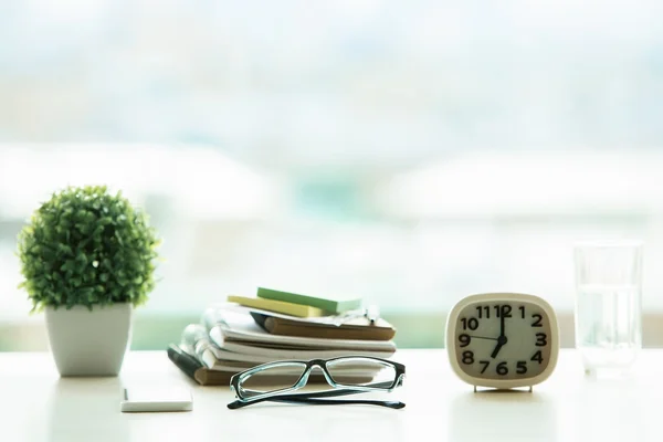 Nahaufnahme eines hellen Desktops mit Brille, Stapel von Lehrbüchern, dekorativer Pflanze, Wasserglas und Uhr auf verschwommenem Hintergrund. Bildungskonzept — Stockfoto