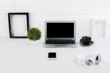 Boş dizüstü bilgisayar ekranı, resmi çerçeveler, kulaklıklar, kahve fincanı, akıllı telefon ve tuğla duvar arka plan üzerinde bitki ile yaratıcı tasarımcı işyeri ön görünümü. Alay etmek