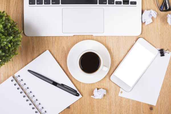 Vista superior del lugar de trabajo desordenado con teléfono inteligente blanco en blanco, taza de café, bolas de papel arrugado, artículos de papelería, teclado portátil y planta. Prepárate. — Foto de Stock