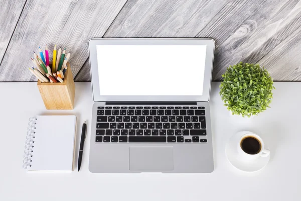 Diseño creativo de escritorio con portátil blanco en blanco, bloc de notas, bolígrafo, lápices, taza de café y planta sobre fondo de madera. Prepárate. —  Fotos de Stock