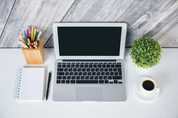 Diseño creativo de escritorio con portátil en blanco, bloc de notas, bolígrafo, lápices, taza de café y planta sobre fondo de madera. Prepárate. —  Fotos de Stock