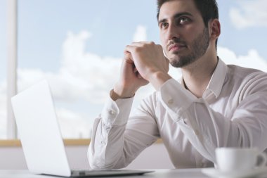 Dizüstü bilgisayar ve kahve fincanı ile ofis masasında hayal yakışıklı genç adam Portresi